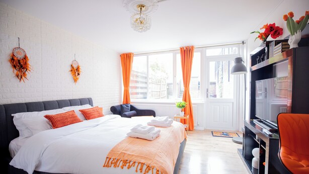 Et godt oplyst soveværelse med en stor seng, orange gardiner og udsigt til det fri.