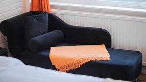 En mørkeblå sofa med et orange pled, placeret foran et vindue med orange gardiner.