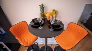 Spisebord med to orange stole, to vinglas, en skål med frugt og en ananas.