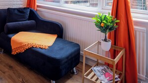 Et værelse med en mørkeblå sofa, et orange pled og en lille træsidebord med en plante, samt orange gardiner.