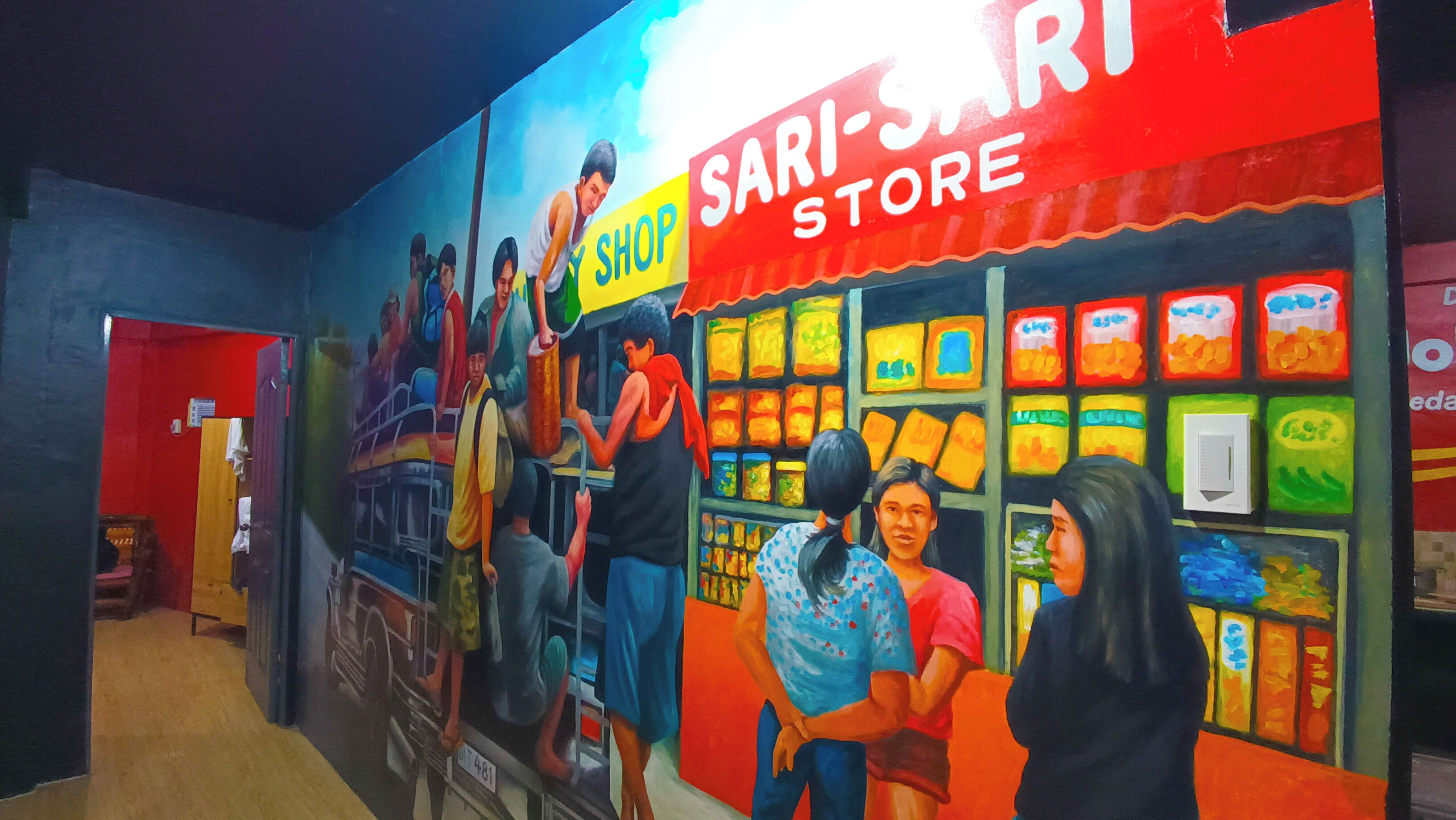 Un murale raffigura un negozio di sari con persone che fanno acquisti e un uomo che suona il tamburo.
