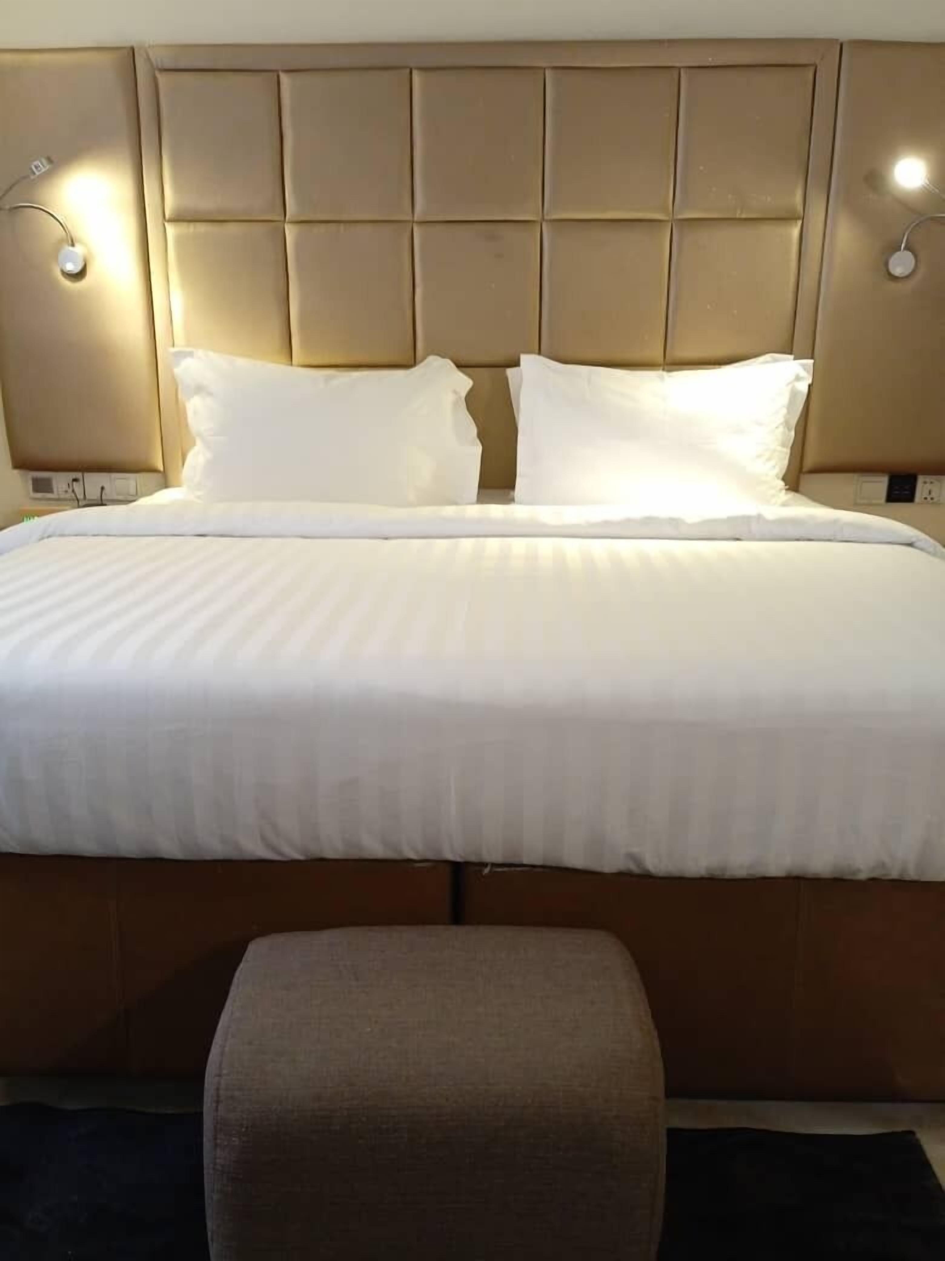 A hotel room with a large bed, two bedside lamps, and a bench at the foot of the bed.