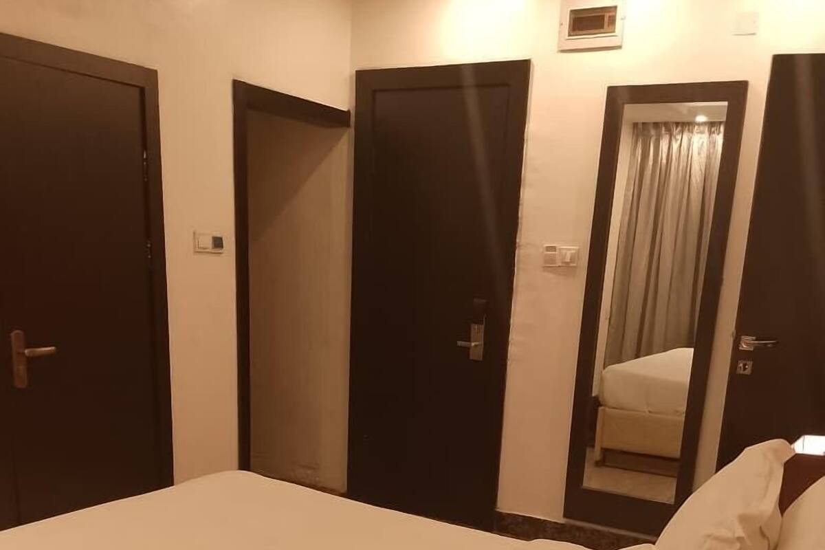 A hotel room with a large bed, two doors, a small window with curtains, and a mirror on the wall.
