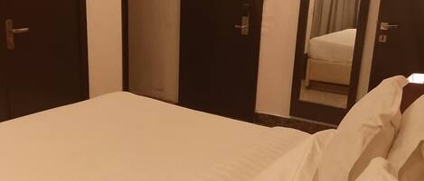 A hotel room with a large bed, two doors, a small window with curtains, and a mirror on the wall.