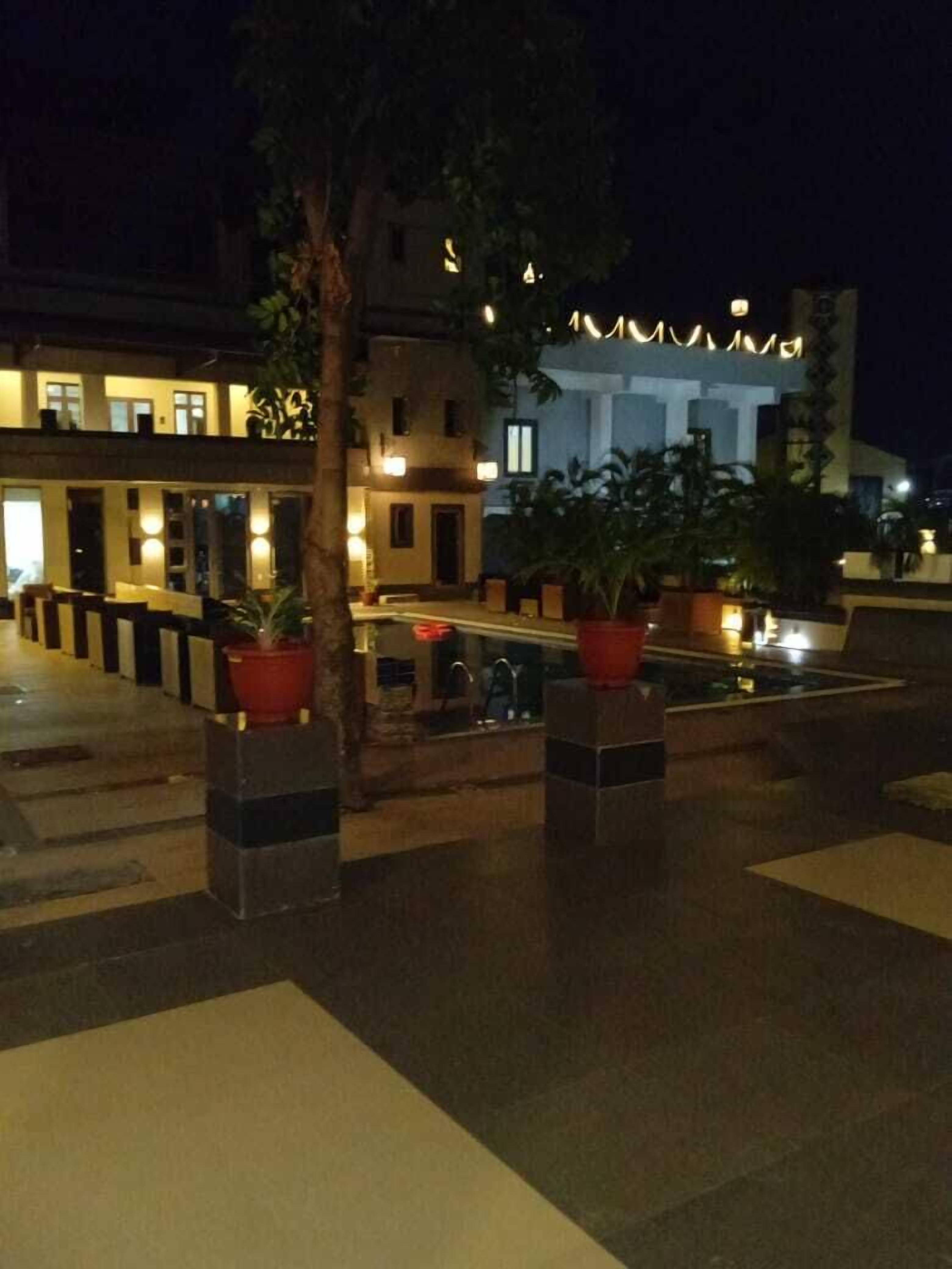 Un espacio al aire libre con plantas en macetas, una piscina y edificios al fondo.