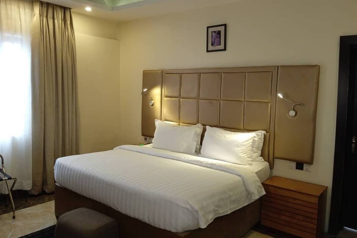 A hotel room with a large bed, a headboard with integrated lighting, a bedside table, and a small wooden cabinet.