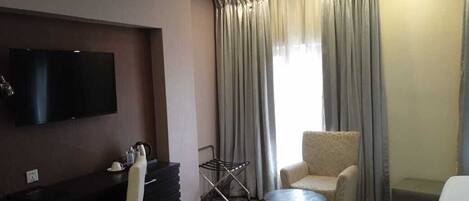 Une chambre d’hôtel équipée d’un téléviseur à écran plat, d’un canapé, d’un fauteuil, d’une petite table ronde et d’un lit.