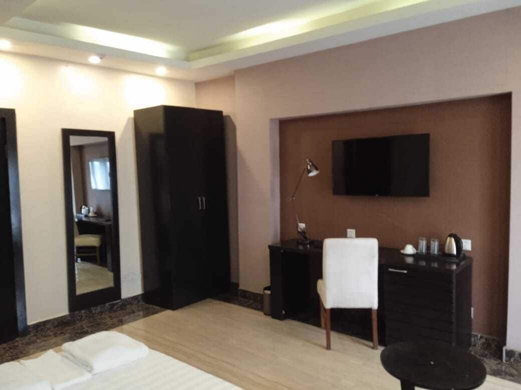 A hotel room with a bed, a desk, a chair, a television mounted on the wall, and a wardrobe.