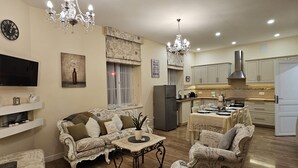 A spacious living room with ornate white furniture, a chandelier, and a modern kitchen in the background. - The Paris Gîte (Ribérac)