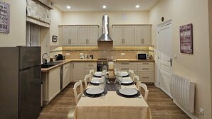 A modern kitchen with a dining area, featuring a chandelier, wooden cabinets, and a central island. - The Paris Gîte (Ribérac)