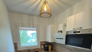 A compact kitchen with a built-in dishwasher, a coffee maker, a microwave, and a toaster. - Large modern F3 - near port (Courseulles-sur-Mer)