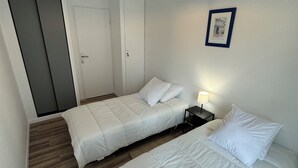 A hotel room with two beds, a ceiling fan, a framed picture on the wall, and a door. - Large modern F3 - near port (Courseulles-sur-Mer)
