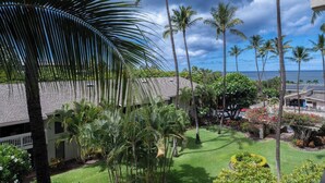A tropical resort with palm trees, a well-maintained lawn, and a view of the ocean.