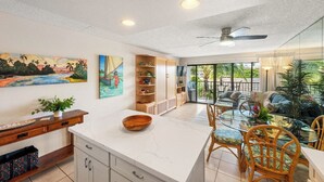 A spacious kitchen with a central island, a dining area with chairs, a ceiling fan, and a view of the outdoors.