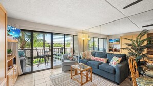 A spacious living room with a grey sofa, a wooden coffee table, and a balcony with outdoor furniture.