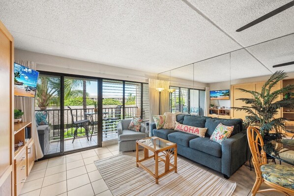 A spacious living room with a grey sofa, a wooden coffee table, and a balcony with outdoor furniture.