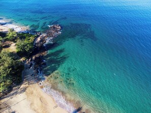 An aerial view of a coastal area with clear turquoise waters, sandy beach, and rocky outcrops.