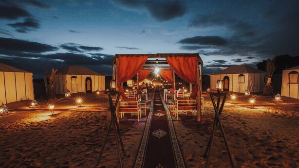 A desert camp with tents, a central seating area with a carpet, and ambient lighting.