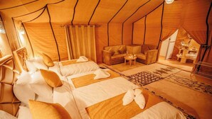 A tent-style room with two beds, a sofa, and a small table with a lamp.