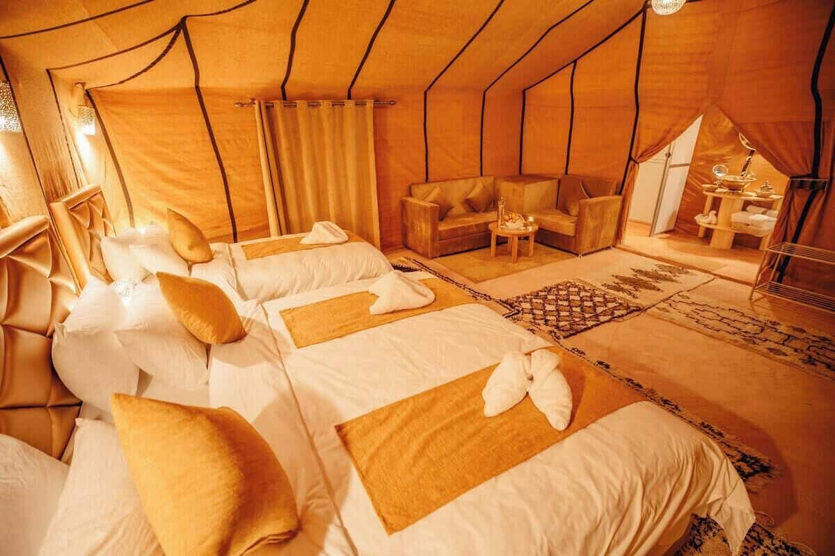 A tent-style room with two beds, a sofa, and a small table with amenities.