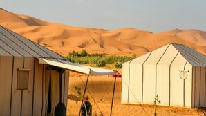 A desert camp with tents and a canopy, surrounded by sand dunes.