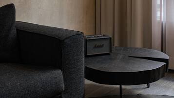 Un salon moderne avec un canapé foncé, une table basse ronde, un amplificateur Marshall et un luminaire suspendu.