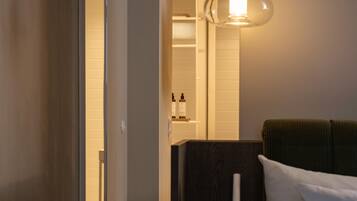 A hotel room with a bed, a nightstand, a lamp, and a bathroom visible through an open door.