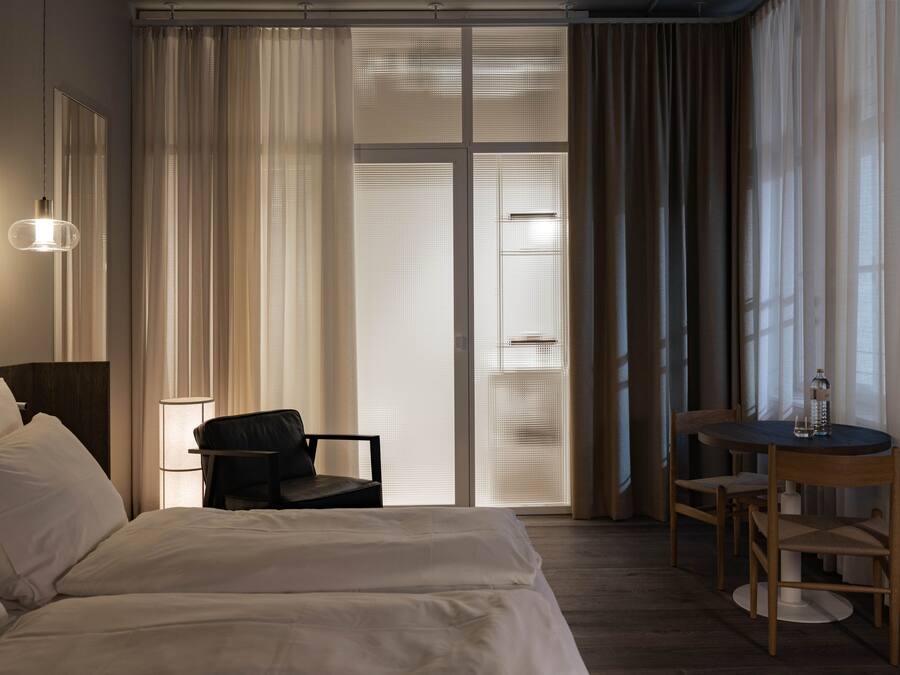 A hotel room with a bed, a chair, a table, and a lamp.