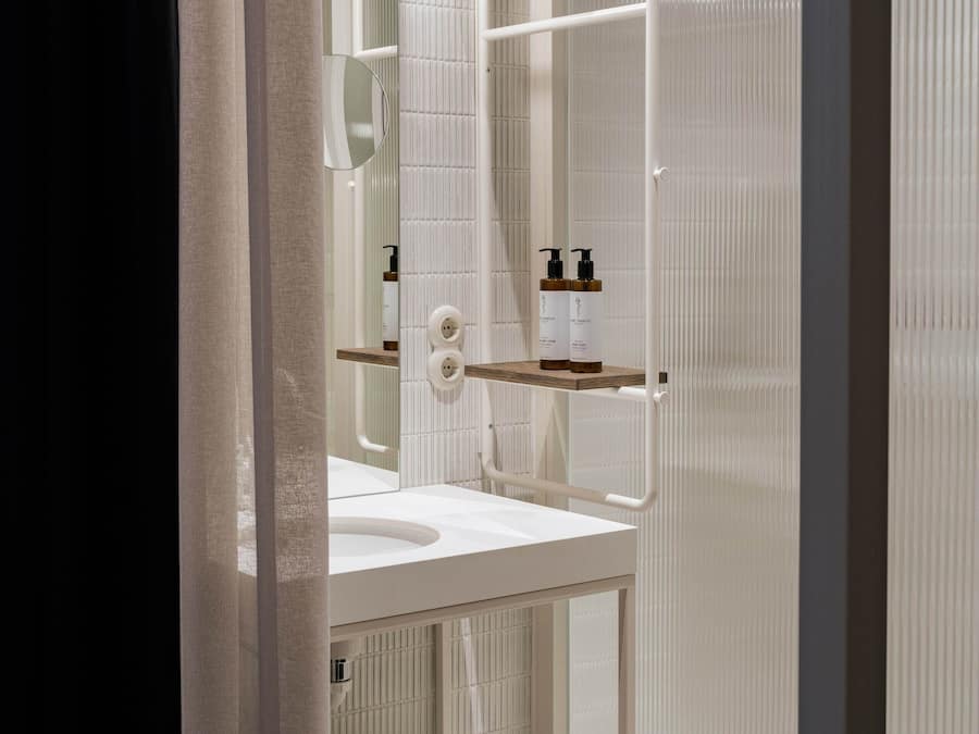 A modern bathroom with a white sink, mirror, and shelving unit.