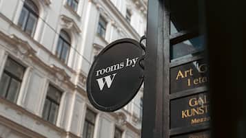 A black sign with "rooms by W" on a building facade.