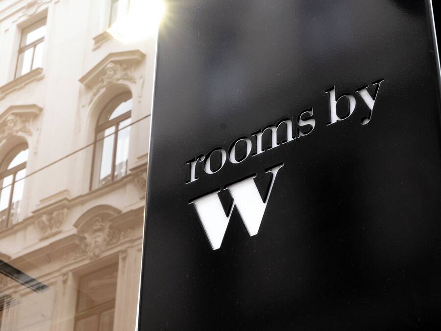 A sign with the text "rooms by W" against a building facade.