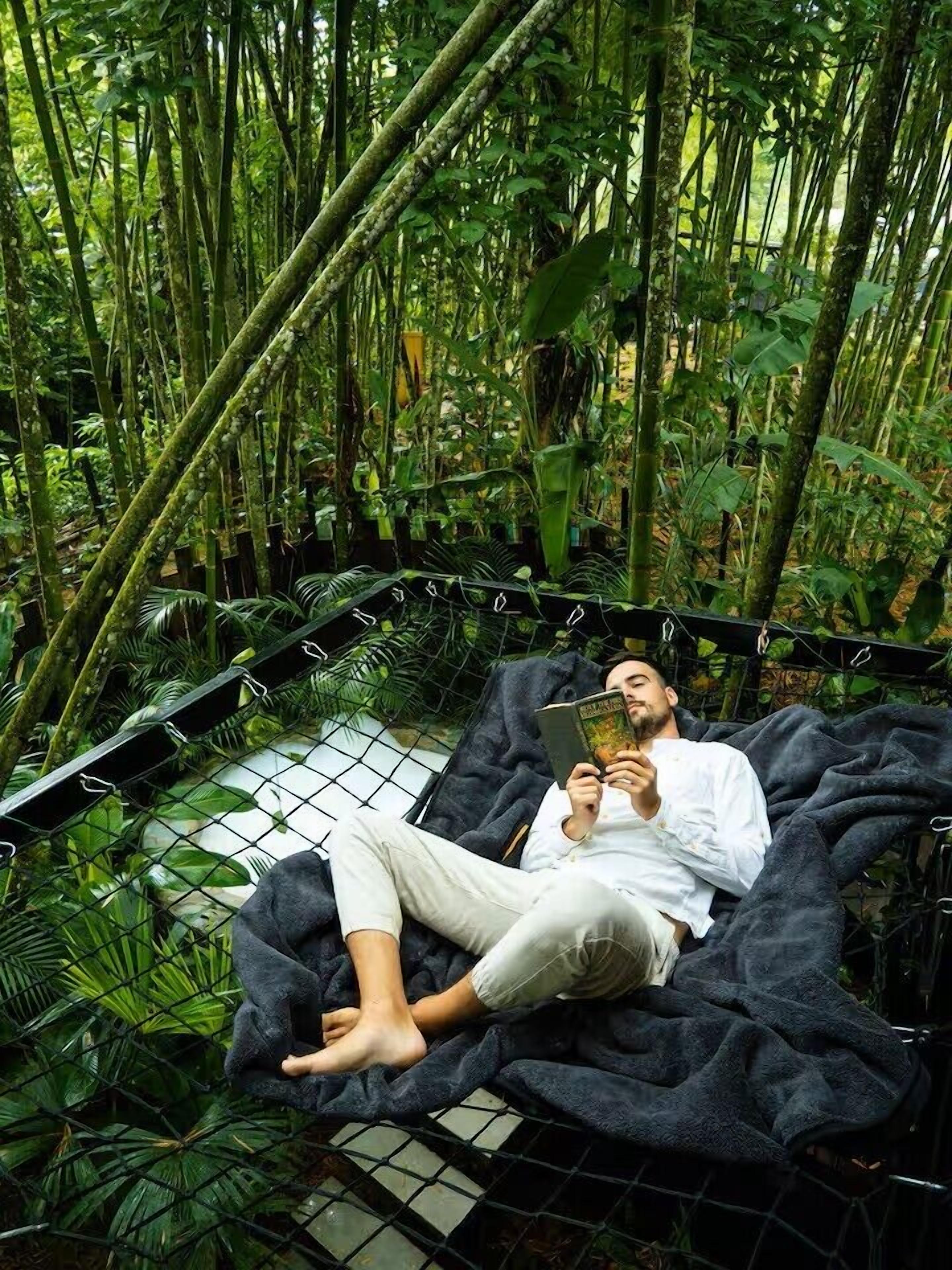 Una persona recostada en una hamaca en un exuberante bosque de bambú verde.