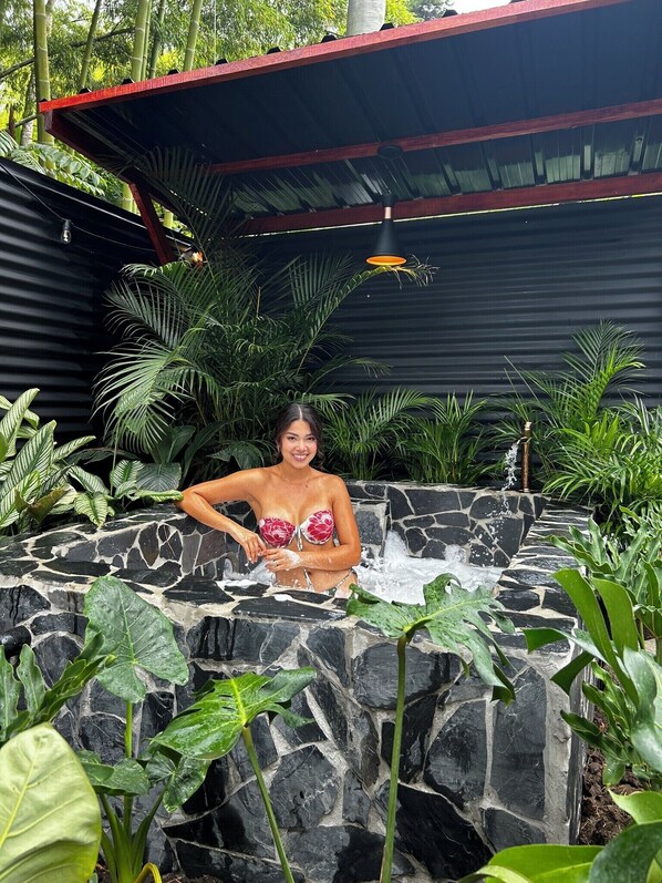 A person relaxing in a hot tub surrounded by lush greenery and a stone wall. - Luna Glamping Salento (Salento)