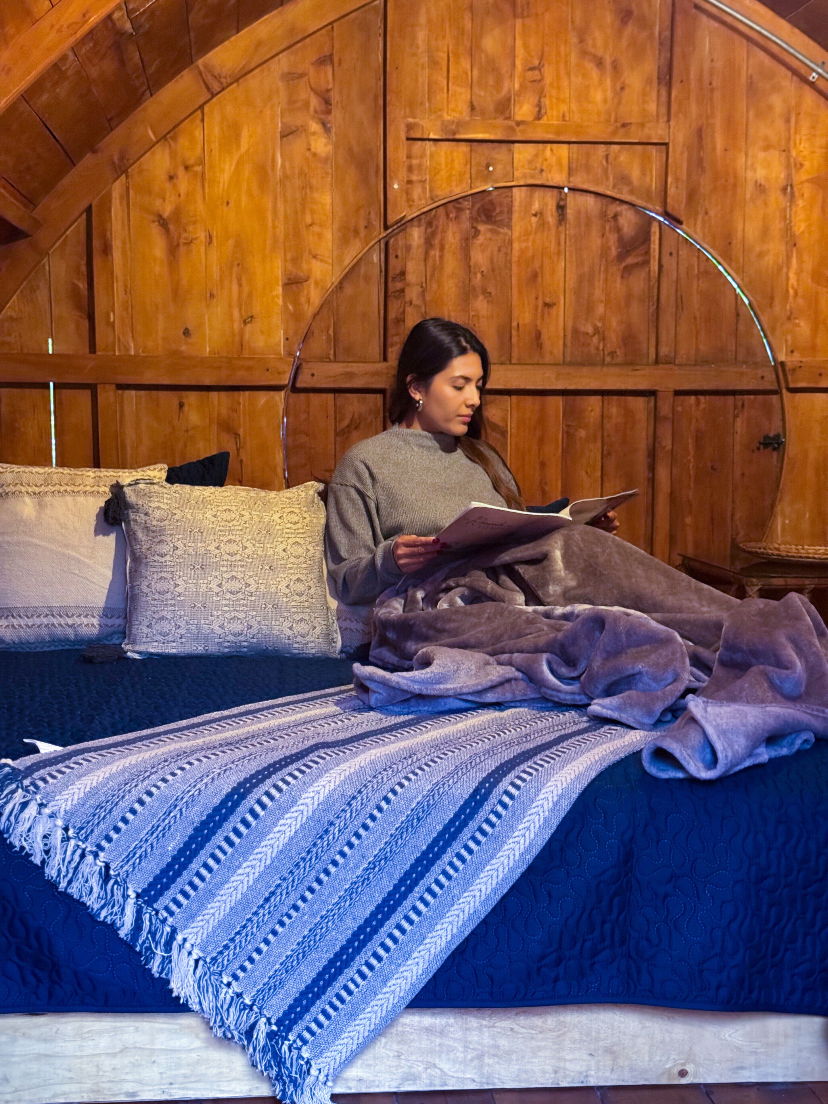 A person sitting on a bed in a room with wooden walls and a curved ceiling.