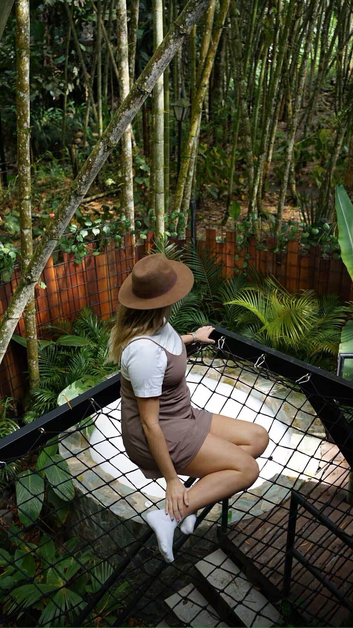 Una persona seduta su un'amaca in un giardino con bambù e diverse piante.