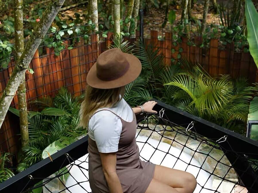 Una persona seduta su un'amaca in un giardino con bambù e diverse piante.