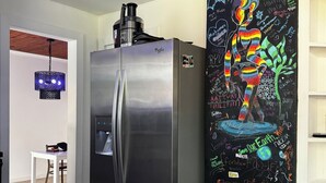 Een keuken met een roestvrijstalen koelkast, een waterdispenser en een prikbord met kleurrijke graffiti en teksten.