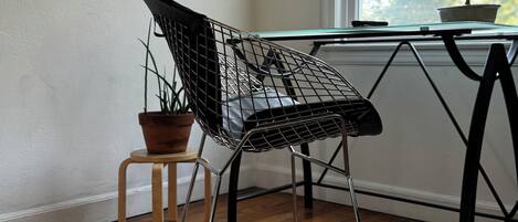 Una silla moderna de estructura metálica y un taburete de madera con una planta en maceta a su lado.