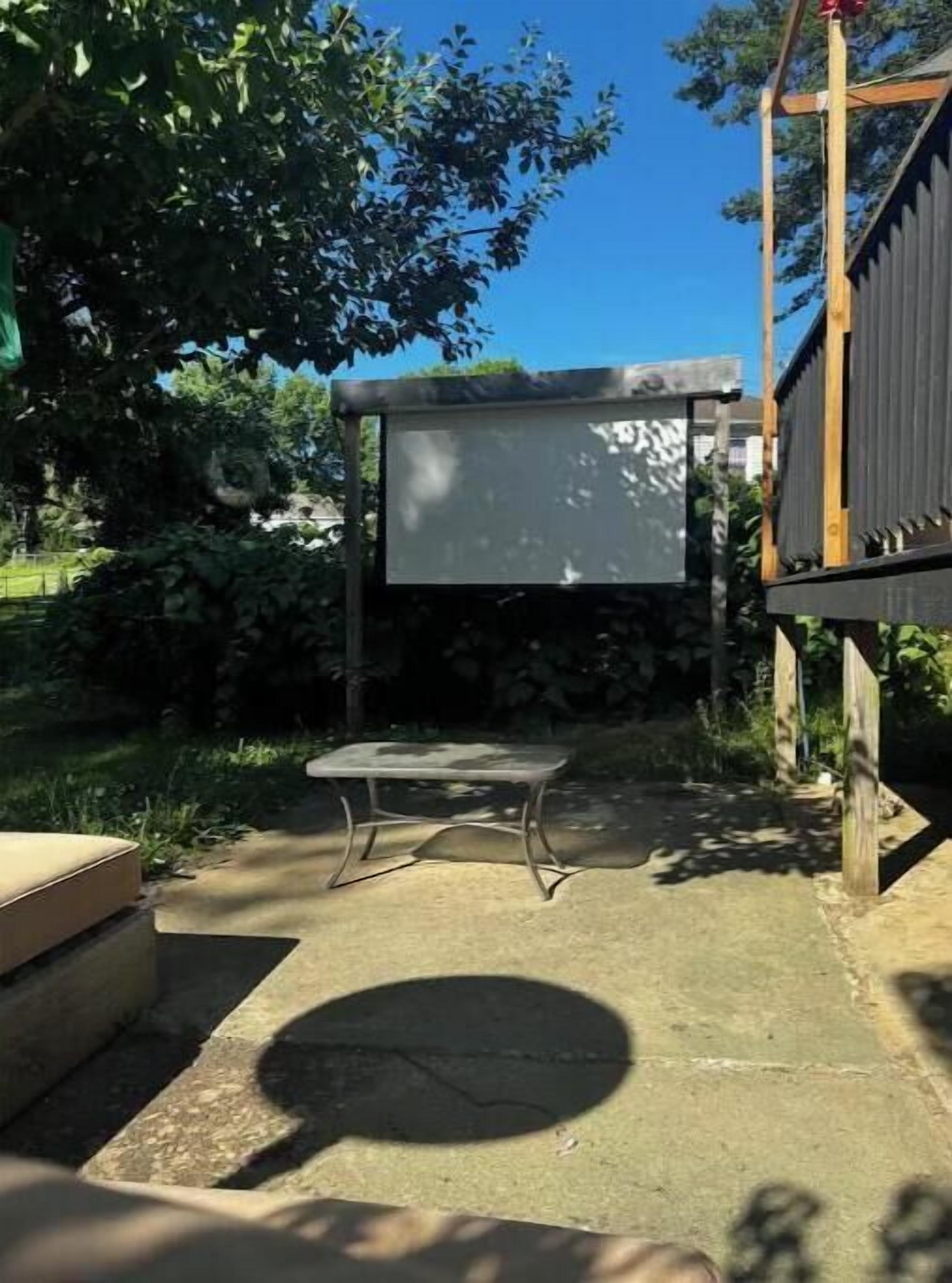 A patio area with a stone table, a wooden bench, and a large screen.
