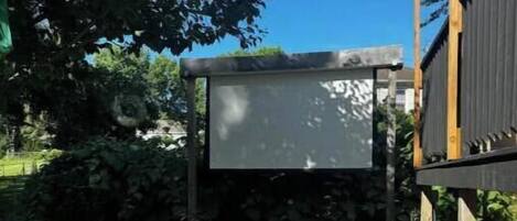 A patio area with a stone table, a wooden bench, and a large screen.