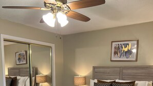 A neatly arranged bedroom with a bed, bedside lamps, a ceiling fan, and a mirror. - East Cobb: Secluded modern chalet with pool (Marietta)