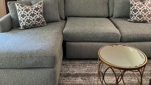 A living room with a gray sectional sofa, patterned throw pillows, a round metal table, and a cityscape painting on the wall. - East Cobb: Secluded modern chalet with pool (Marietta)
