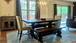A dining area with a wooden table, four chairs, a chandelier, and a view of the outdoors through large windows. - East Cobb: Secluded modern chalet with pool (Marietta)