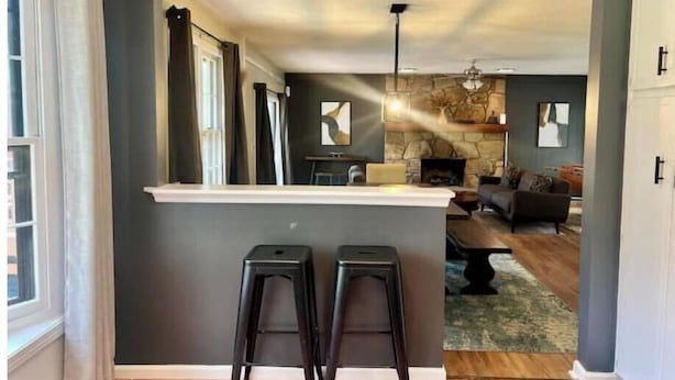 A modern kitchen with a bar area, two stools, and a stone fireplace in the background. - East Cobb: Secluded modern chalet with pool (Marietta)