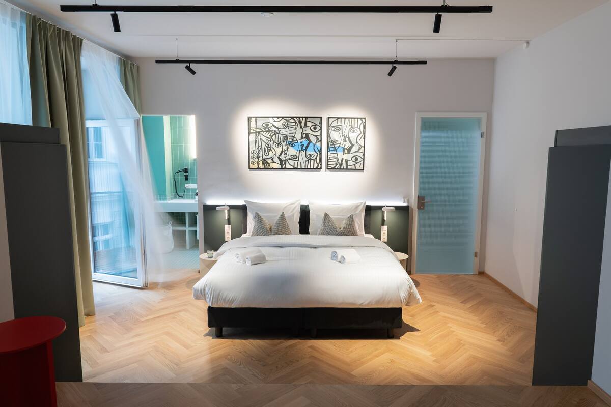 A modern bedroom with a large bed, two wall art pieces, a sliding glass door, and a red accent chair.
