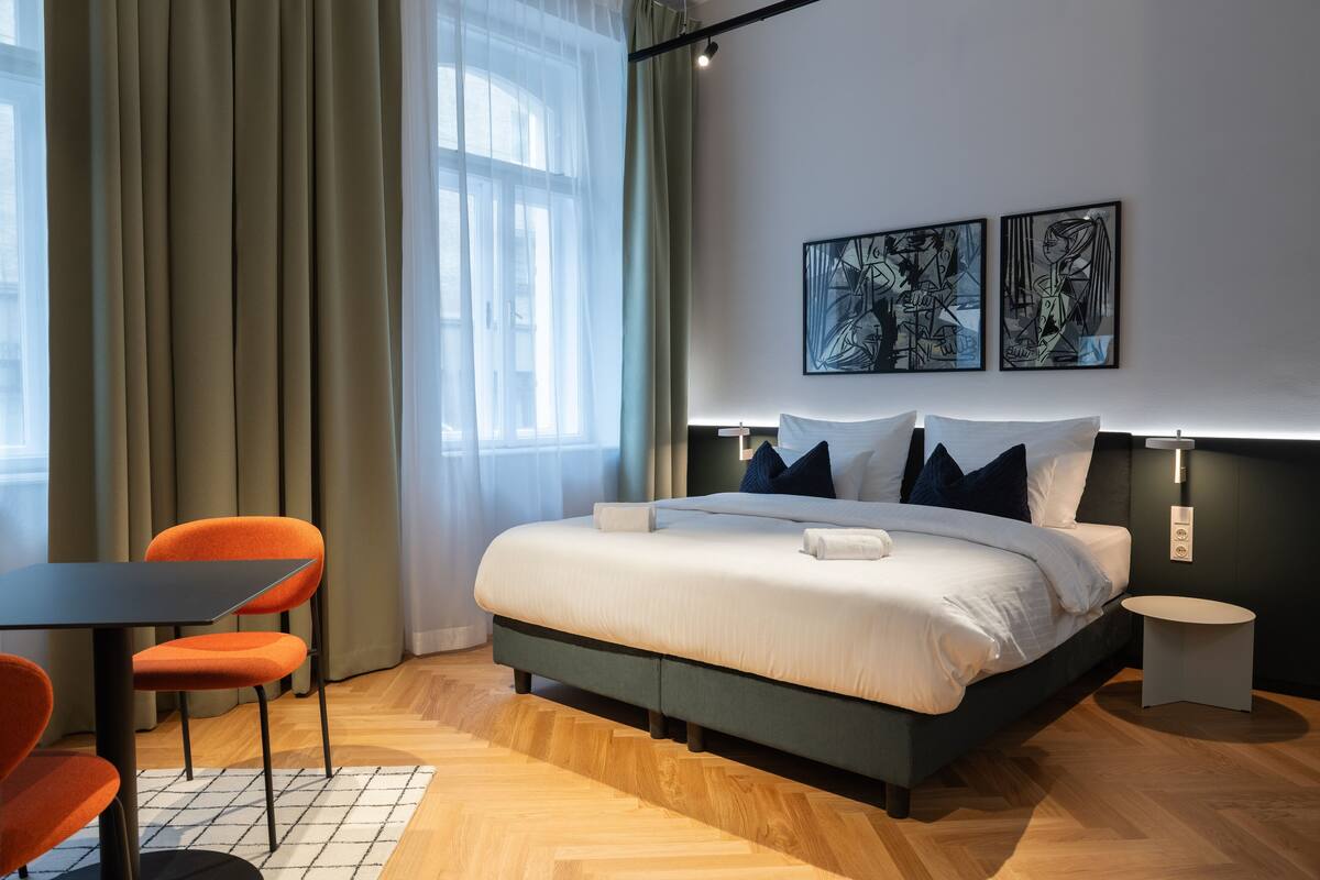 A modern hotel room with a bed, a table, two chairs, and artwork on the wall.