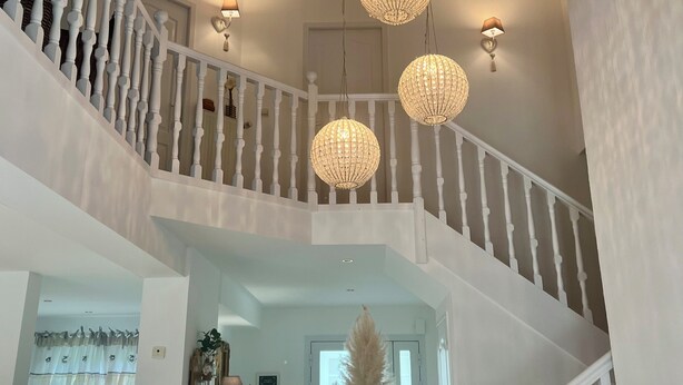 A multi-level interior with a white staircase, chandeliers, and a decorative ceiling piece. - Villa Campagne Chic (Meulers)