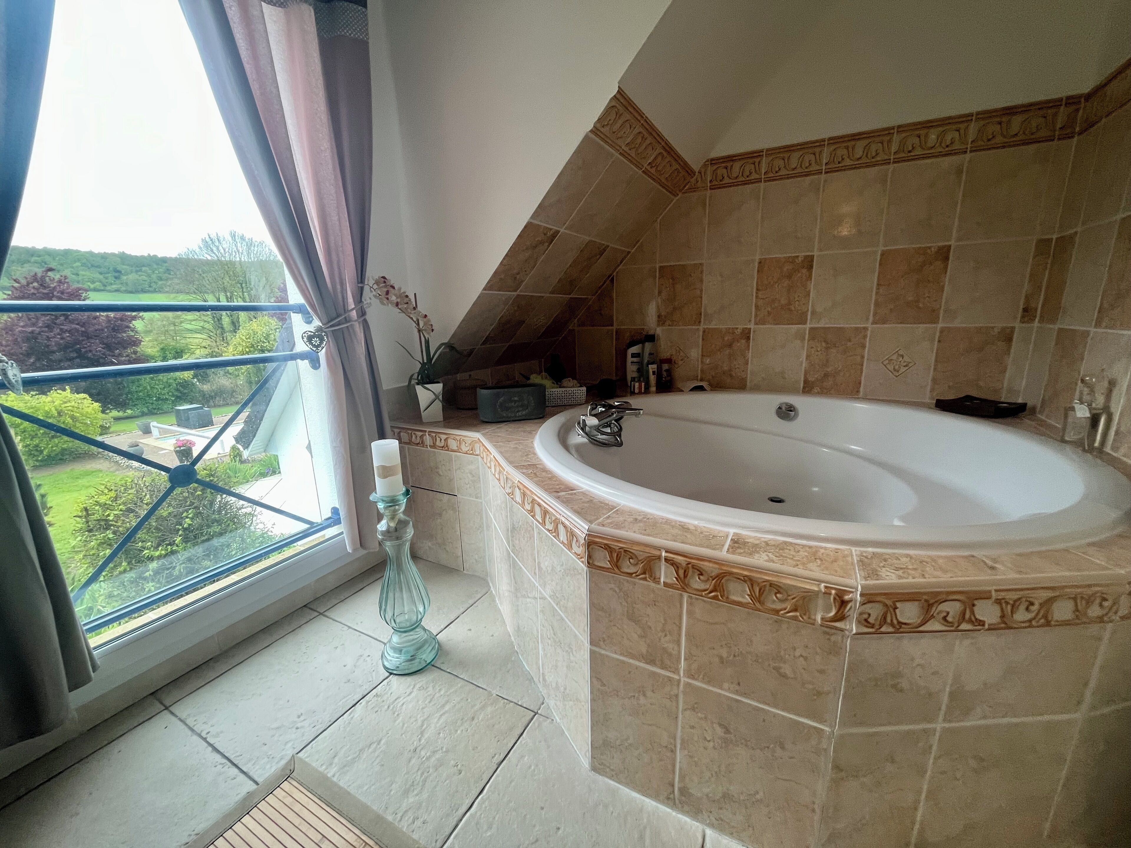 Ein Badezimmer mit einer großen Badewanne, einem Fenster mit Vorhängen und Blick auf Grünfläche.
