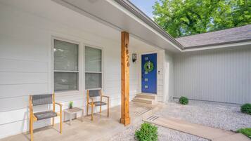 A house with a blue door, two wooden chairs, a small table, and a wooden post with numbers.