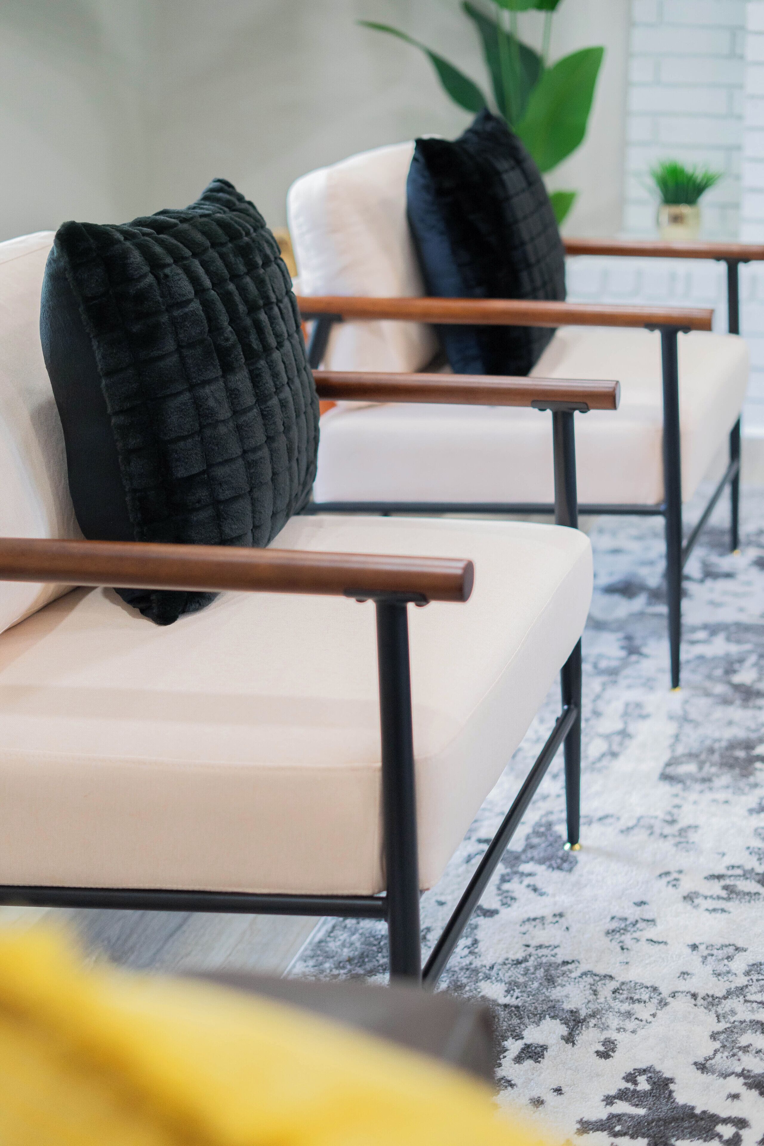 A modern living room with a sofa and armchairs, a patterned rug, and a small plant on a side table.